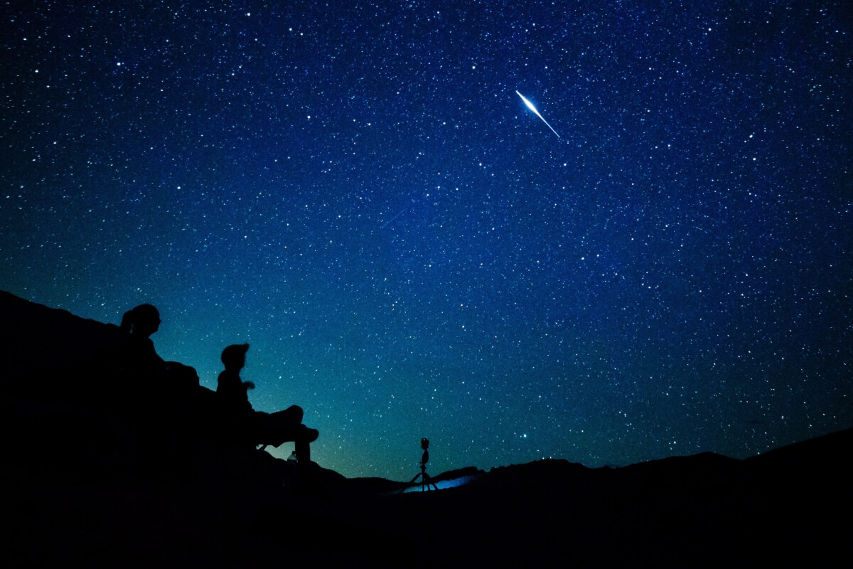 Two people watching the milky way with a shooting star overhead